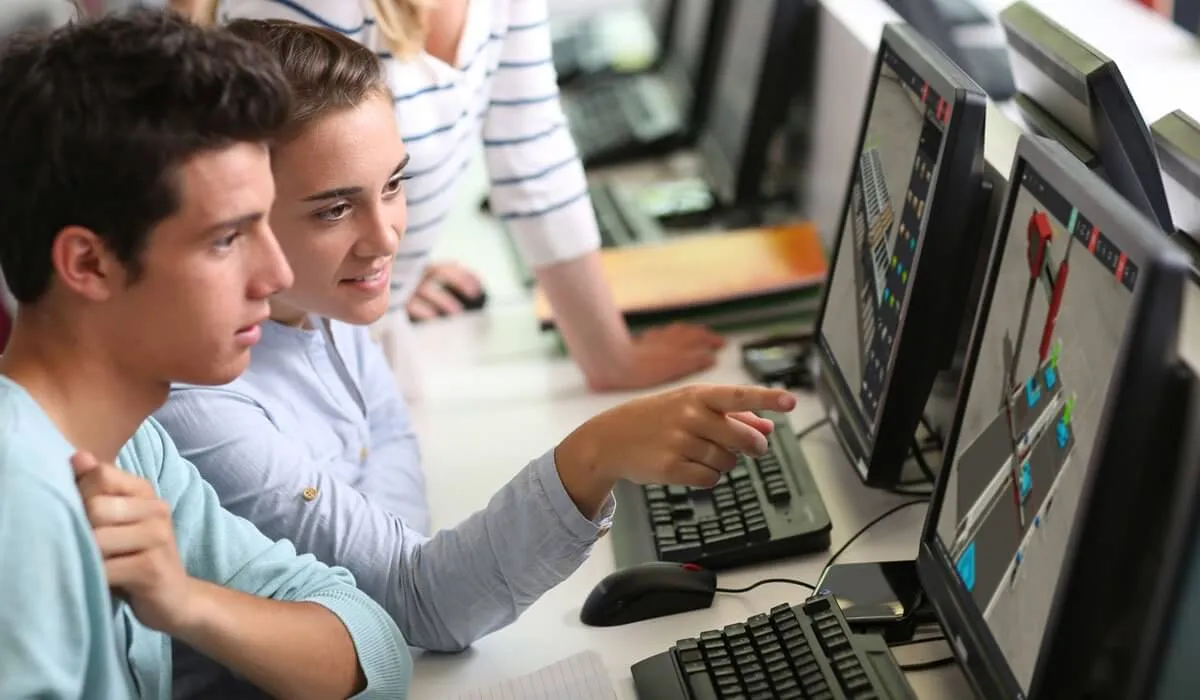 Two students working together at computers running Factory I/O in a classroom